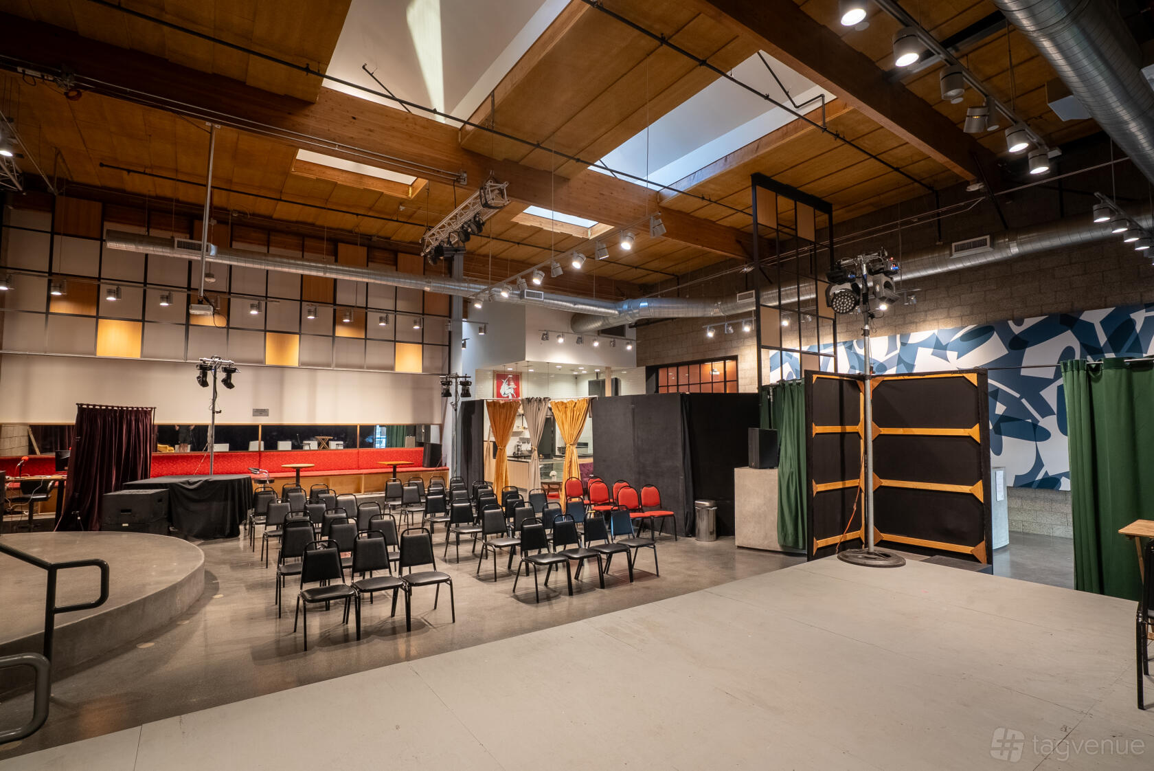 A theatre screening room with stage lighting, rows of black chairs, and exposed wood ceiling at Promenade Playhouse.