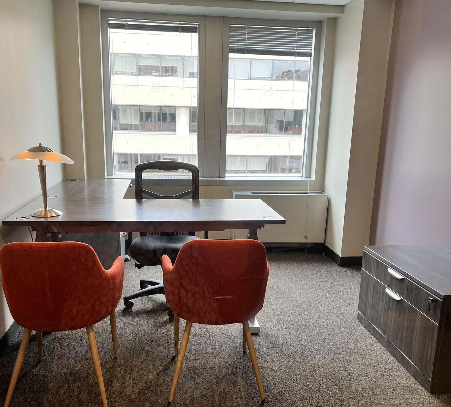 An office space with a wooden desk, two orange chairs, a task chair, and large windows at Intelligent Office.
