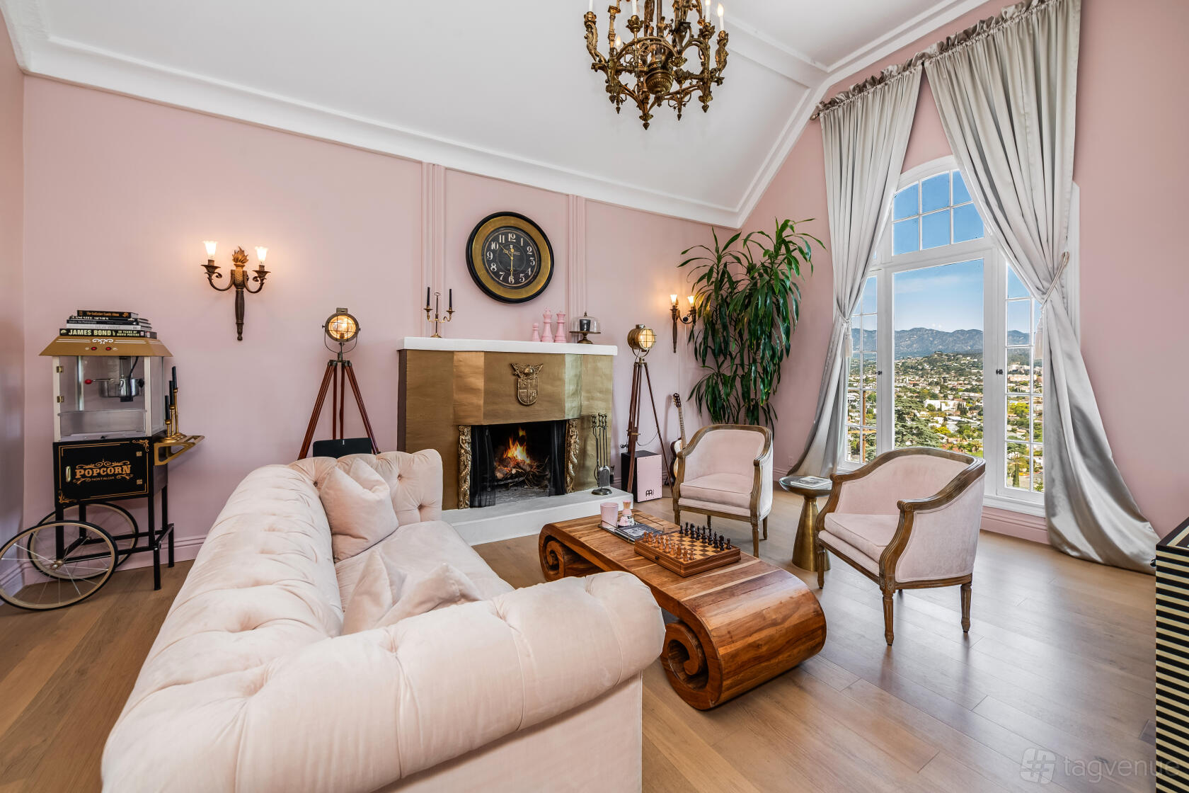 A living room with blush pink walls, a gold fireplace, vintage chandelier, and arched window at La Vie En Rose - Elegant Mansion.