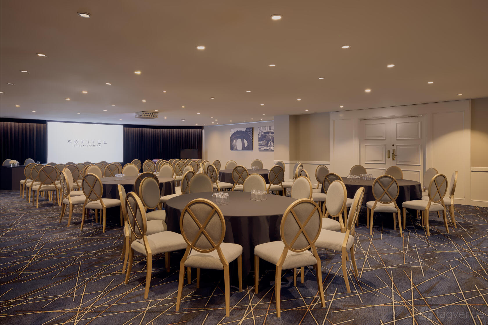 An event space with round tables, upholstered chairs, and a projection screen at Sofitel Brisbane Central.