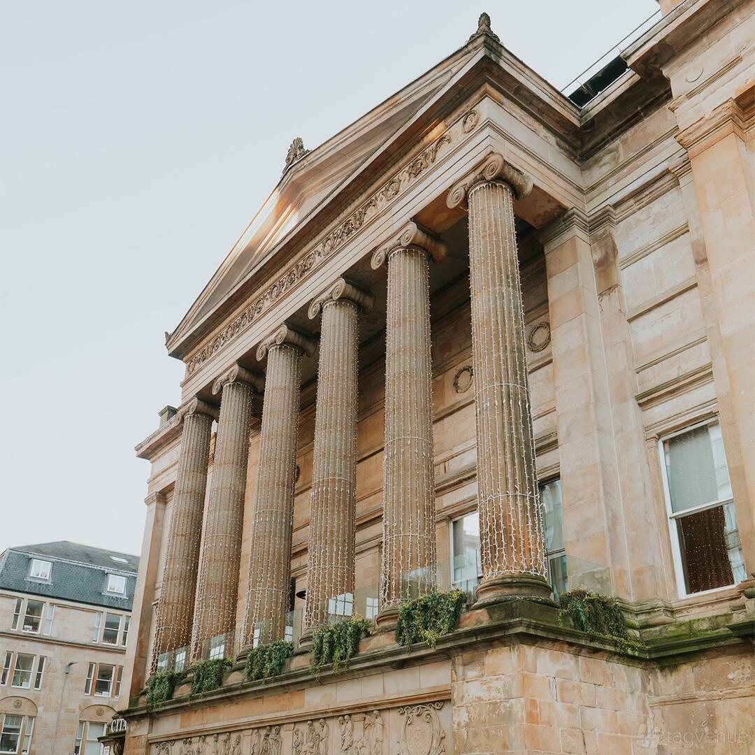 A historic building with grand stone columns draped in string lights at Citation Weddings and Events.