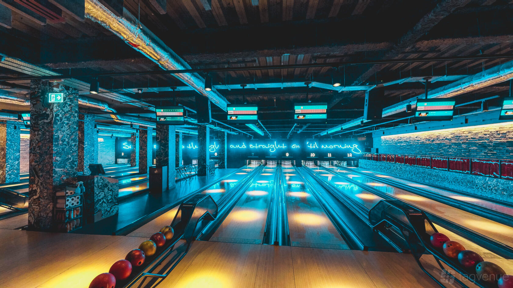 A bowling alley with neon lighting, multiple lanes, digital scoreboards, and exposed ceiling at Queens Skate Dine Bowl.