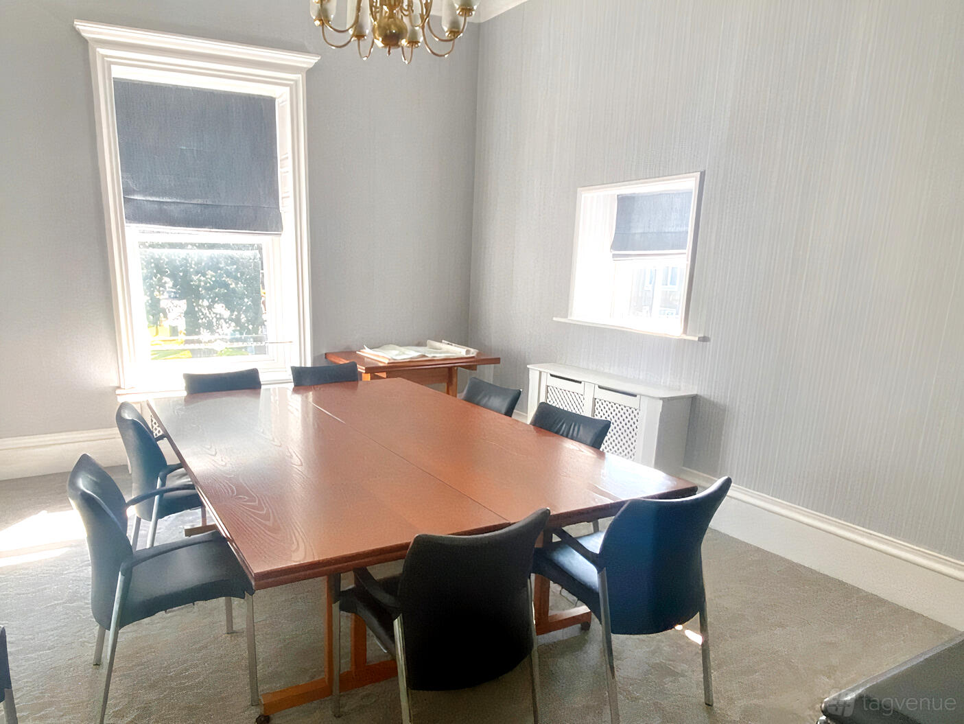 A meeting room with a large wooden conference table, black chairs, and tall windows at Flixton House.