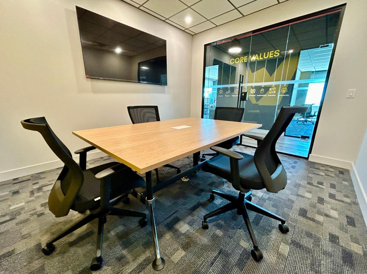A meeting room with a rectangular wooden table, four ergonomic chairs, and a wall-mounted screen at Venture X Etobicoke.