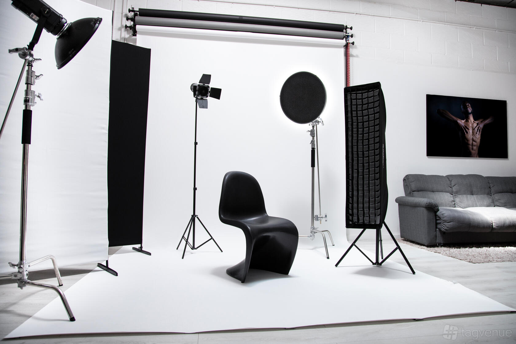 A photo studio with white seamless backdrop, studio lighting equipment, and a black chair at Mons Studio Warehouse.