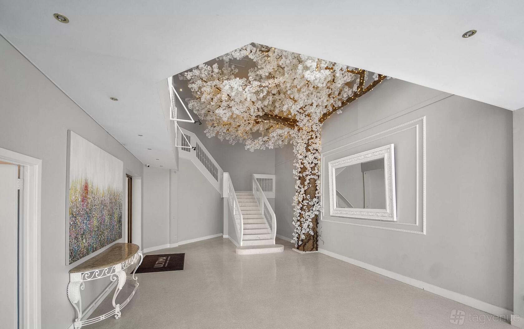 A hall with a white staircase, a decorative tree with white blossoms, and large wall mirrors at Ultima Function Center.