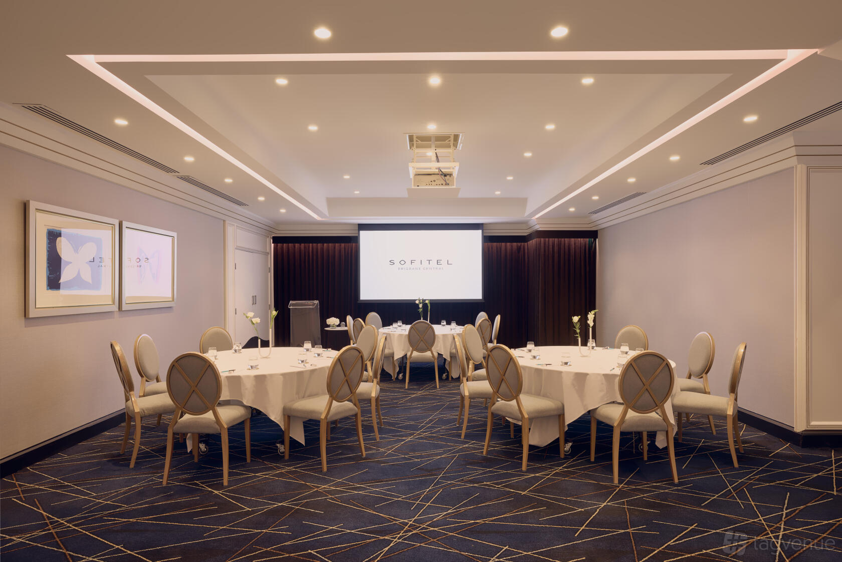 An event space with round tables, white linens, modern chairs, and a projector screen at Sofitel Brisbane Central.