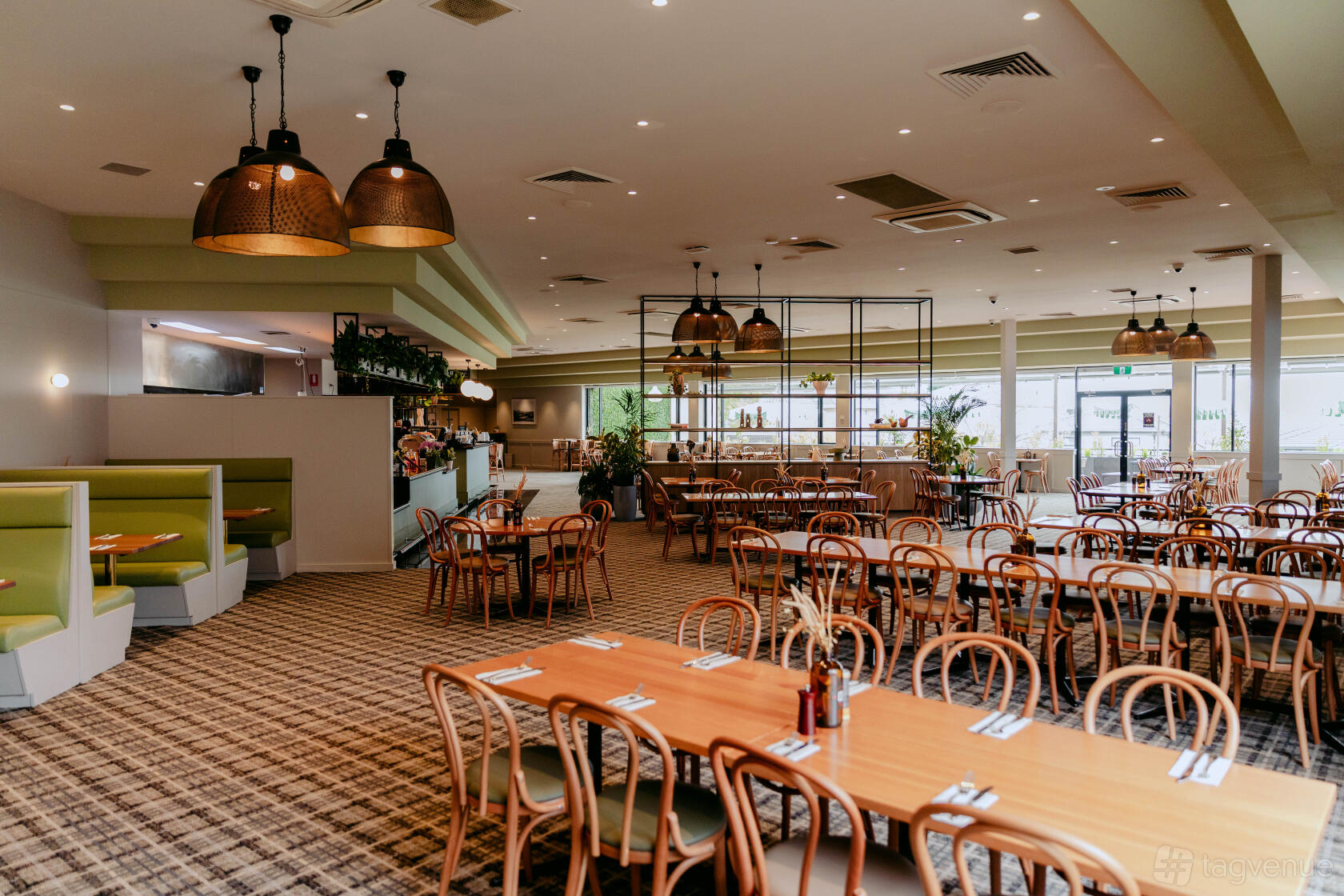 A pub dining space with wooden tables, bentwood chairs, green upholstered booths, and pendant lighting at Cherry Hill Hotel.