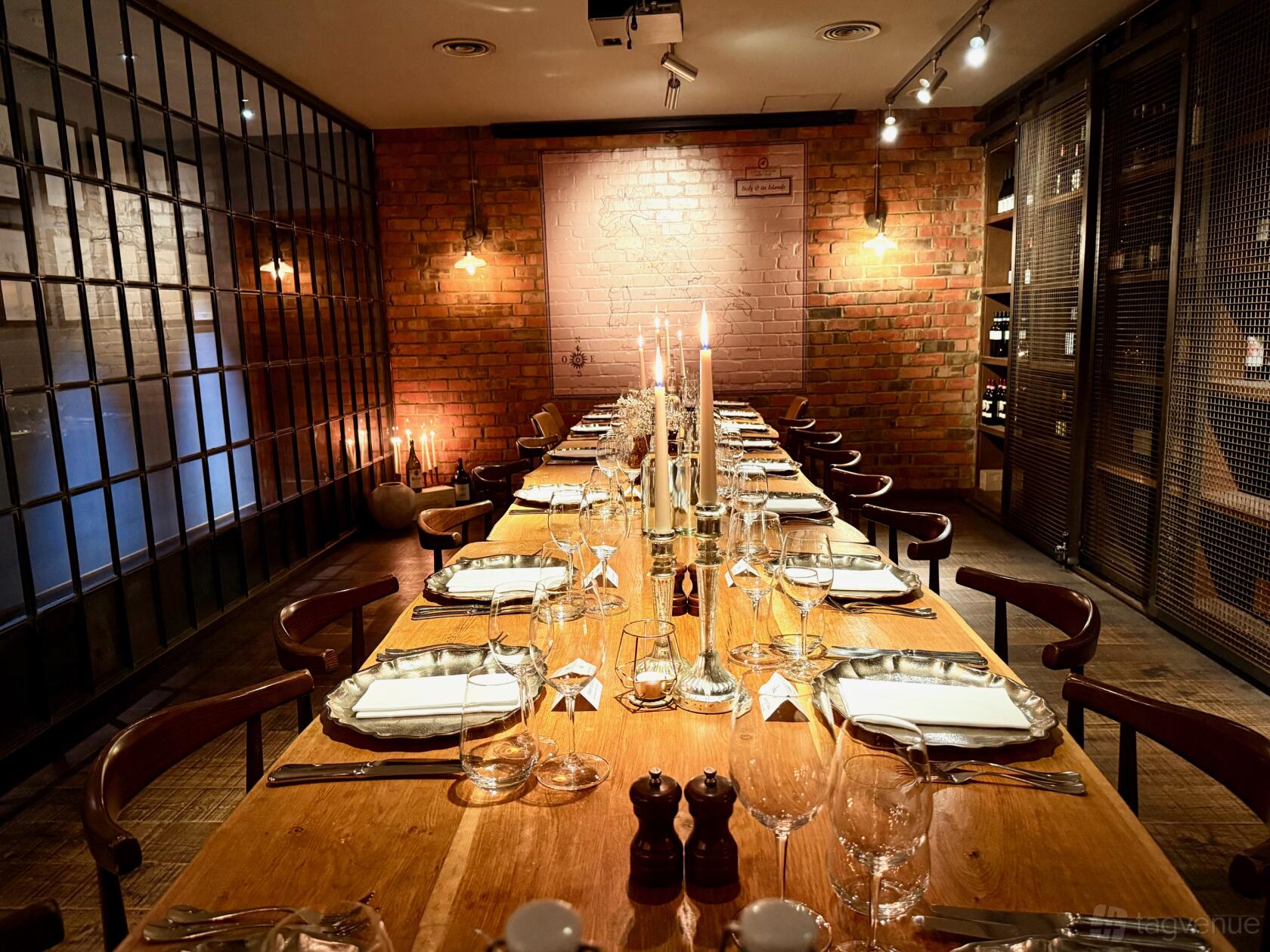A dining room with exposed brick walls, long wooden table, and wine racks at Canto Corvino.