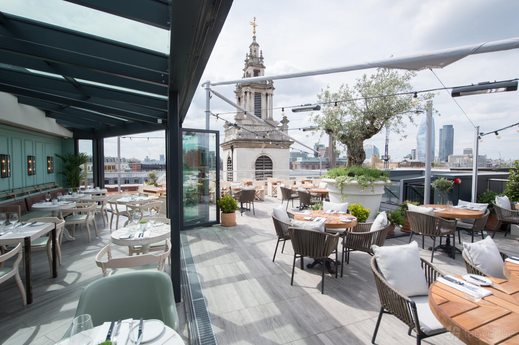 A hotel rooftop with outdoor dining, city views, potted plants, and round tables at Vintry & Mercer.