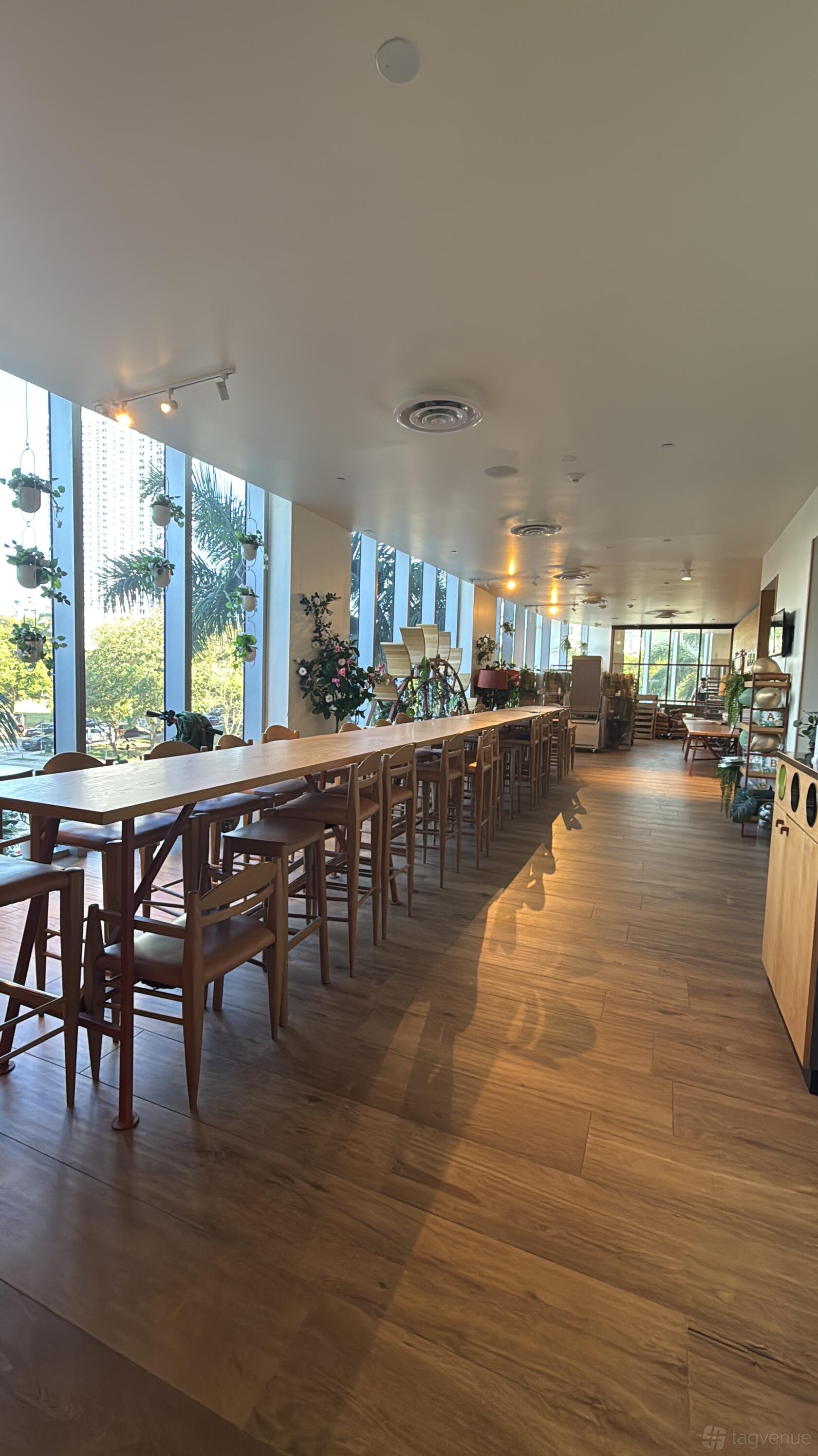 A function room with floor-to-ceiling windows, potted plants, and a long wooden table at Paolo Fontanot Bakery.