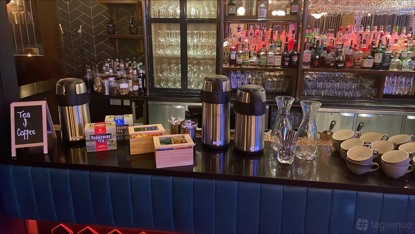 A restaurant bar with a black countertop, tea dispensers, glassware shelves, and liquor bottles at Banyan Newcastle.