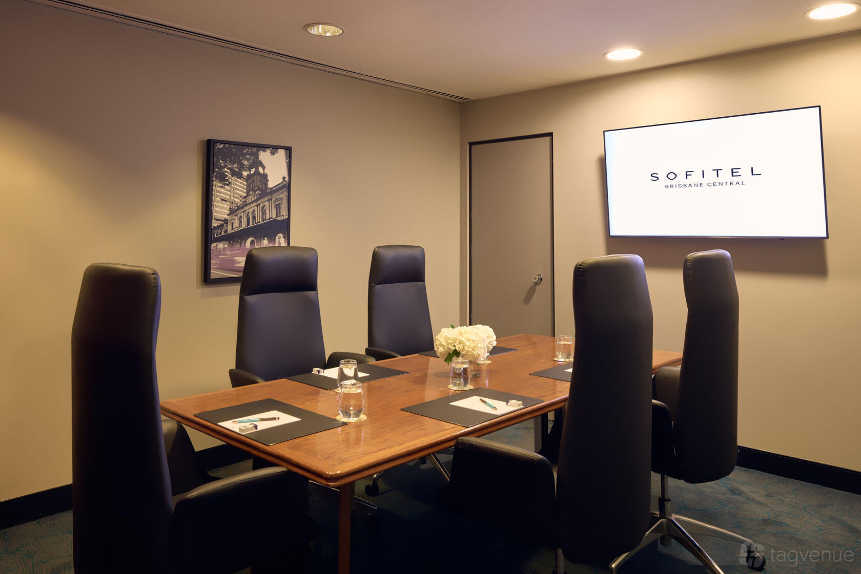 A hotel meeting room with a wooden conference table, six high-back chairs, and a wall-mounted screen at Sofitel Brisbane Central.