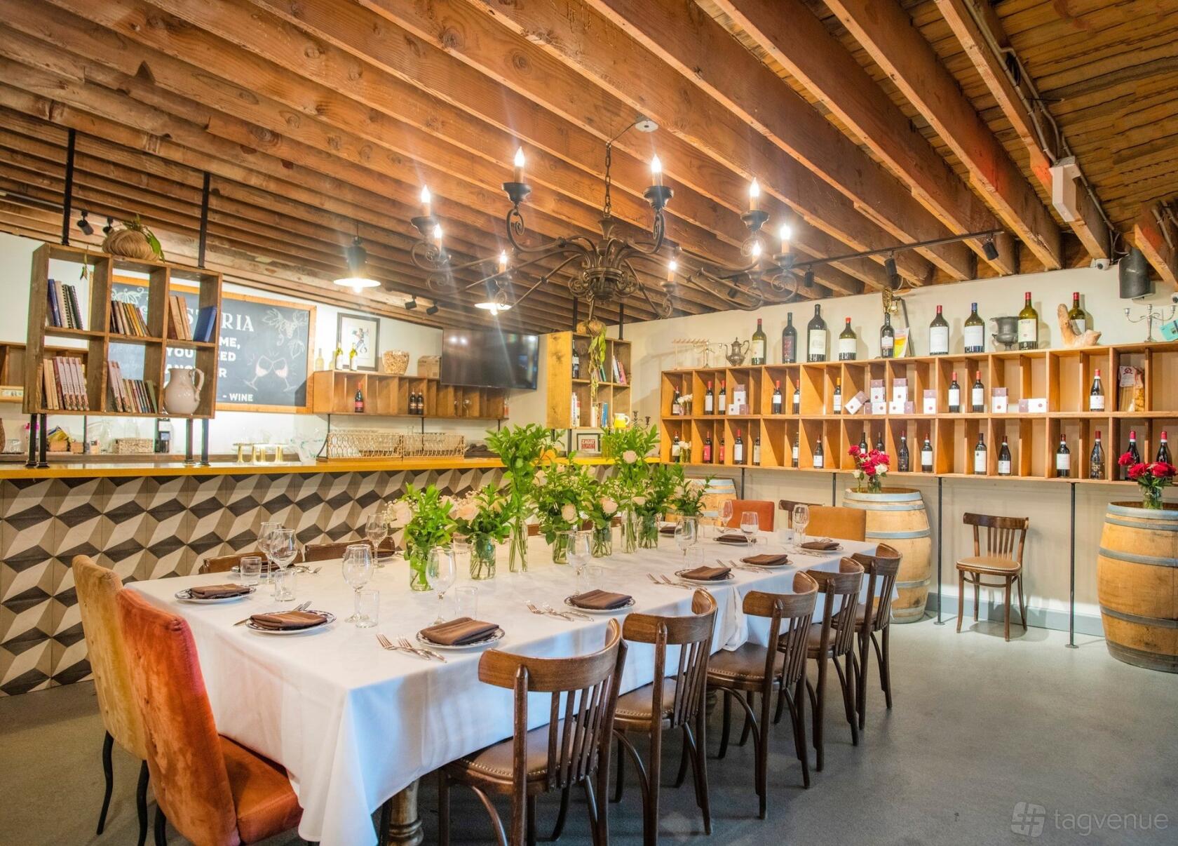 A private dining room with a long table, white tablecloth, wood beam ceiling, and wine bottle display at Osteria Miami Event venue.