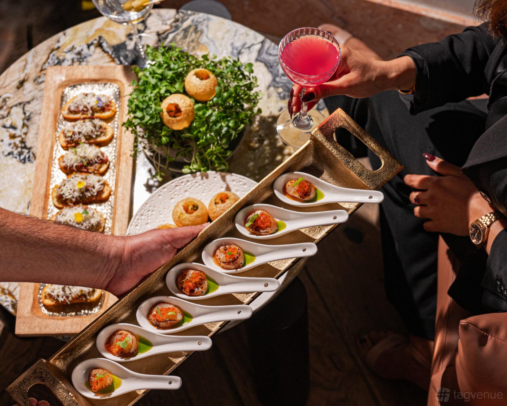A hotel bar with gourmet appetizers served on ceramic spoons and a pink cocktail at Amora Hotel Jamison Sydney.
