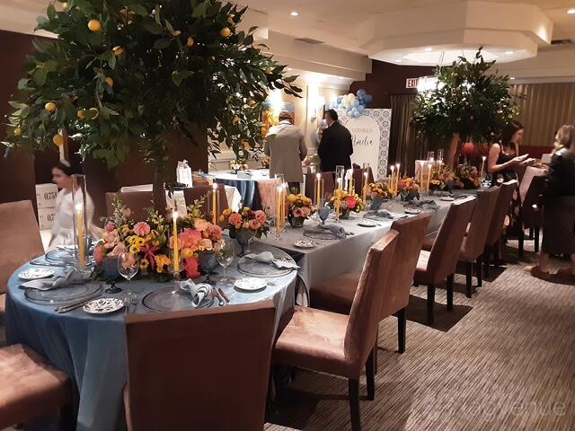 A function room with two long tables, blue linens, floral centerpieces, and candles at La Luce Ristorante.