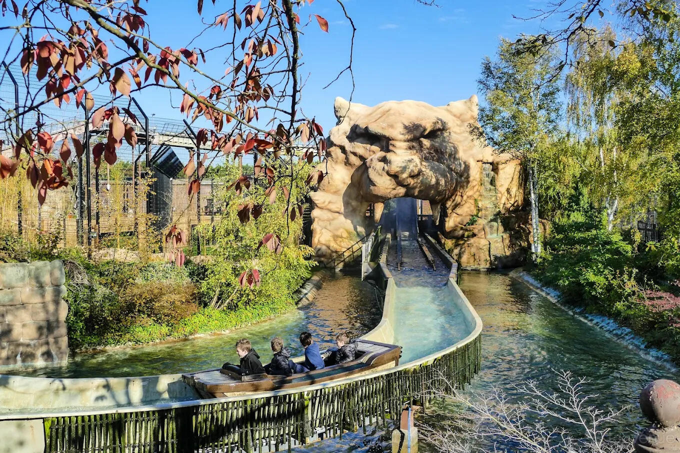An event venue with a log flume ride passing through a giant sculpted face and lush greenery at Chessington World Of Adventures Resort.