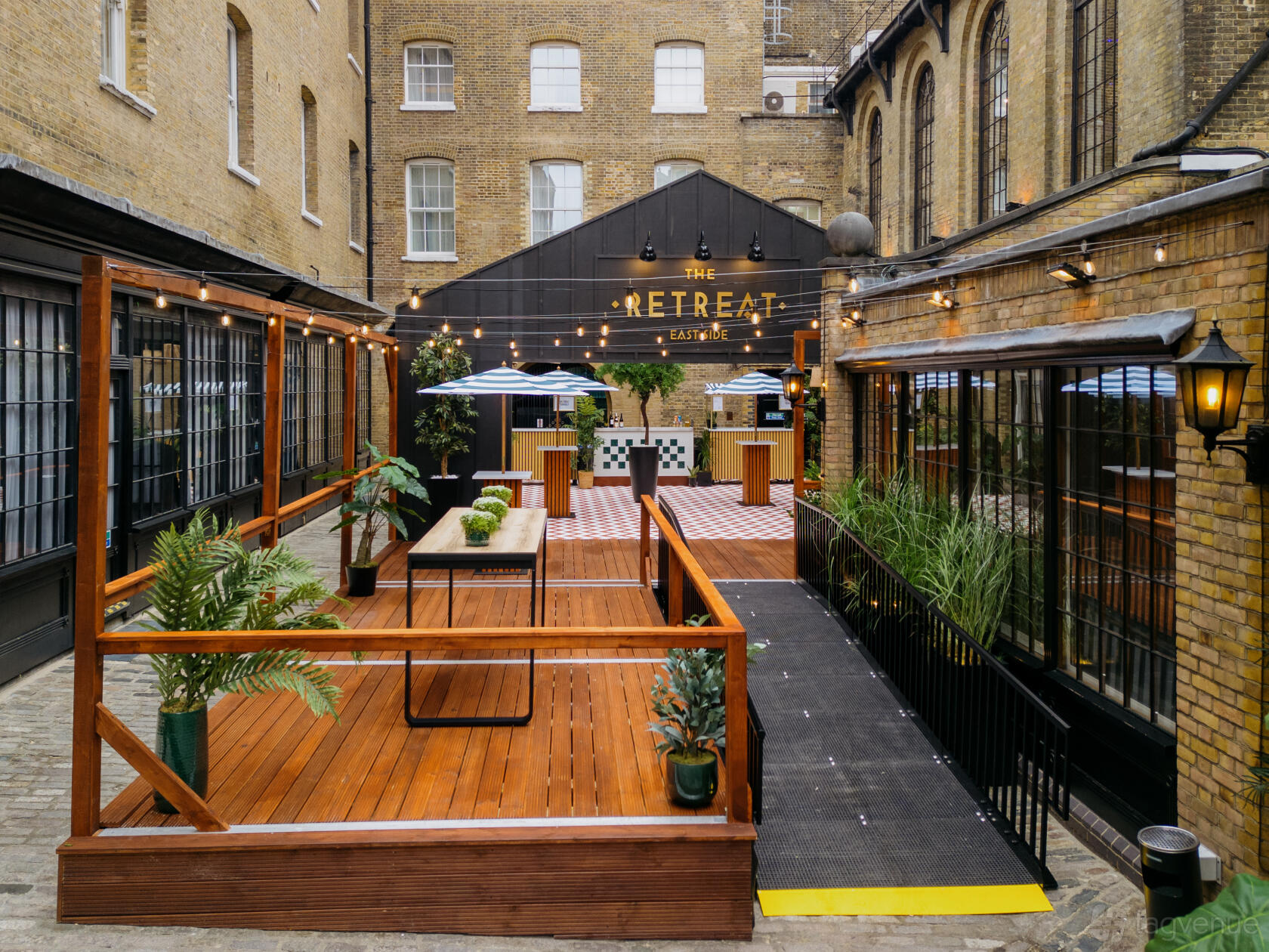A courtyard garden with wooden decking, potted plants, string lights, and outdoor seating at The Brewery.