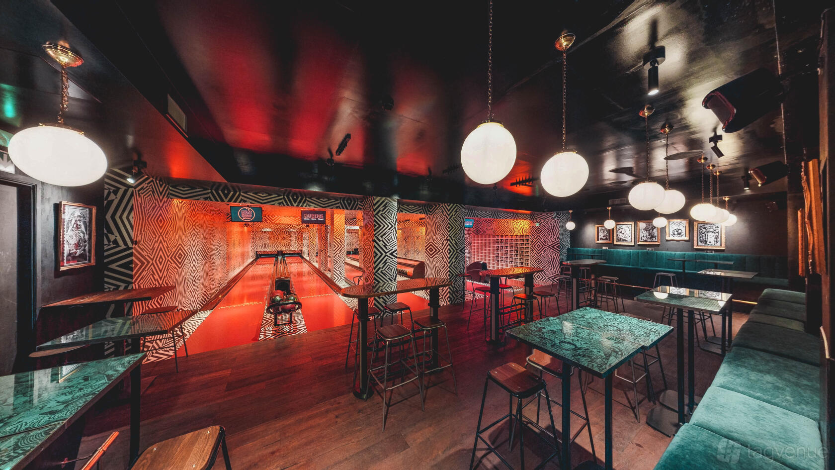 A bowling alley with glowing red lanes, pendant lights, and retro-patterned walls at Queens Skate Dine Bowl.