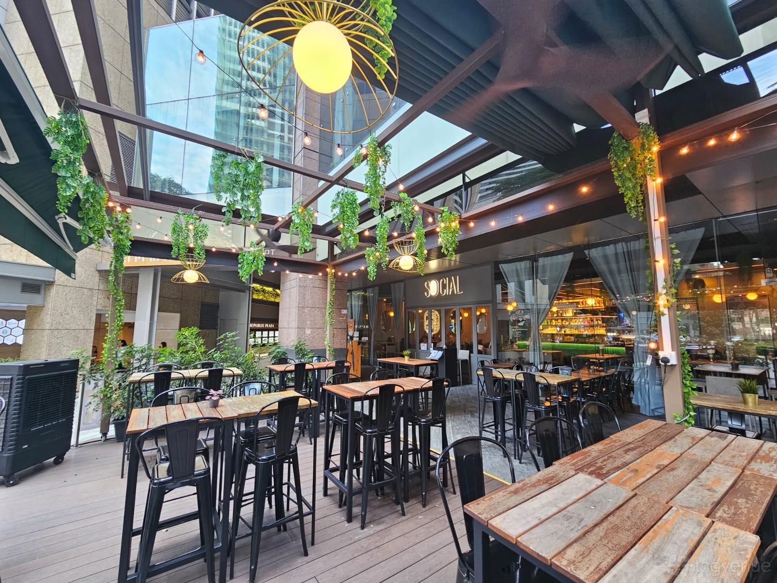 An outdoor bar with wooden tables, hanging greenery, and string lights at Social Bar & Bistro.