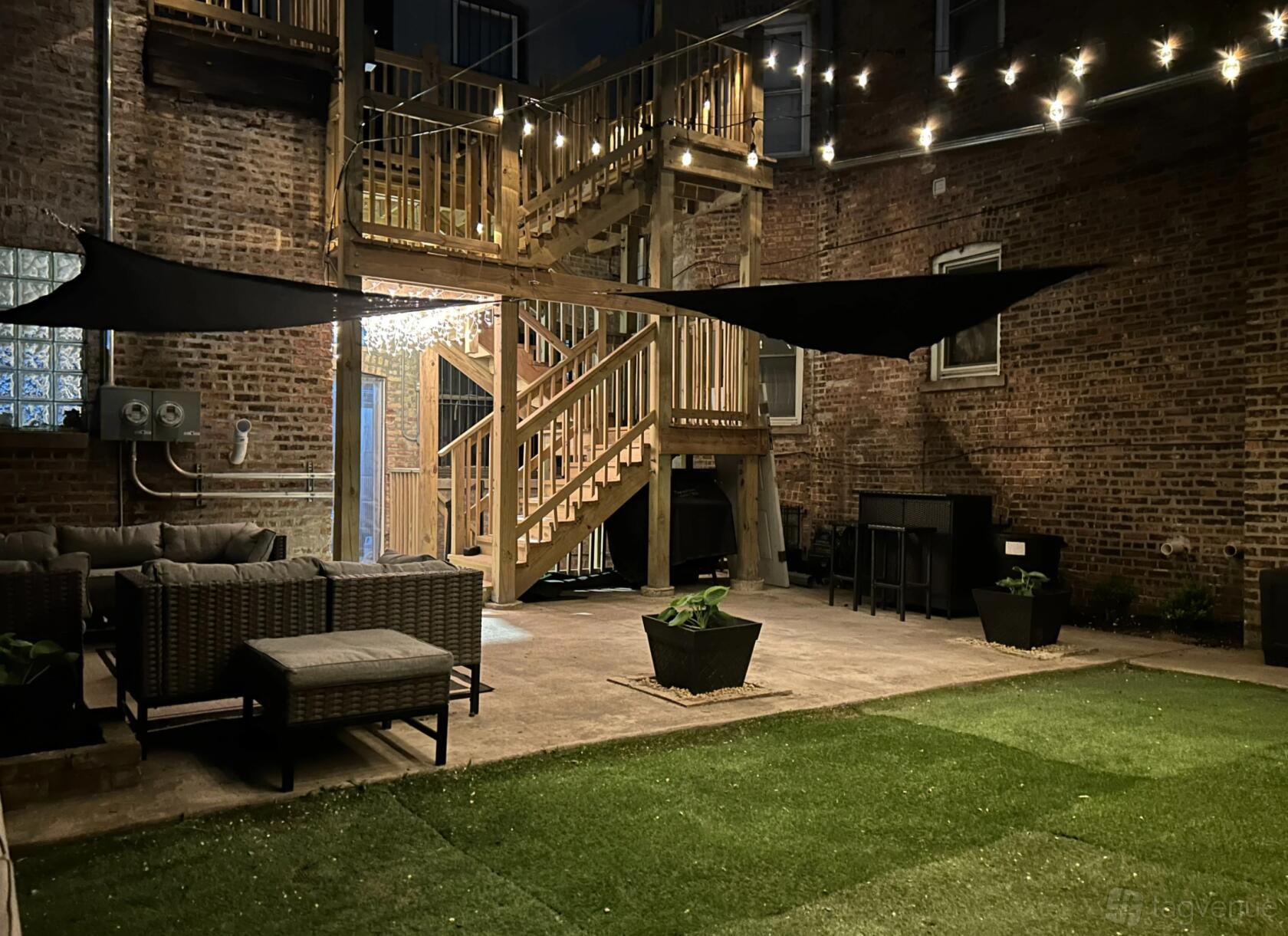 An outdoor lounge with string lights, artificial turf, wicker seating, and exposed brick walls at Thrift LLC.