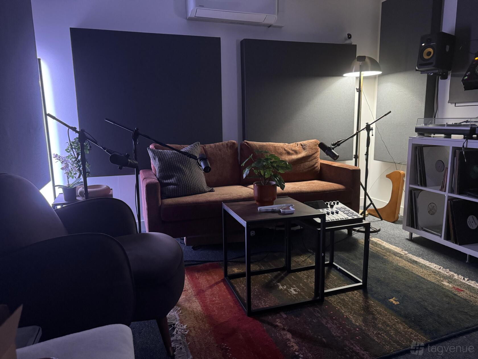 A podcast studio with a brown sofa, microphones on stands, acoustic panels, and a rug at Sourc Studios.