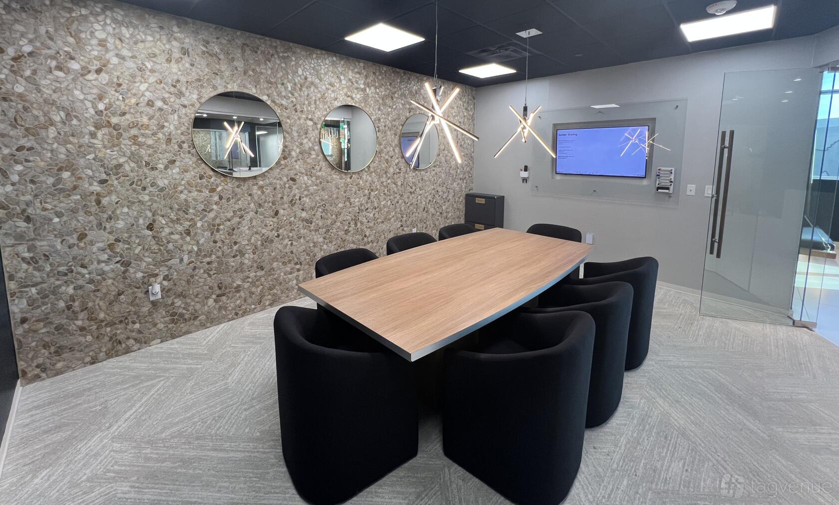 A boardroom with a wood conference table, black chairs, stone accent wall, and pendant lighting at Lucid Private Offices - Allen / Fairview.