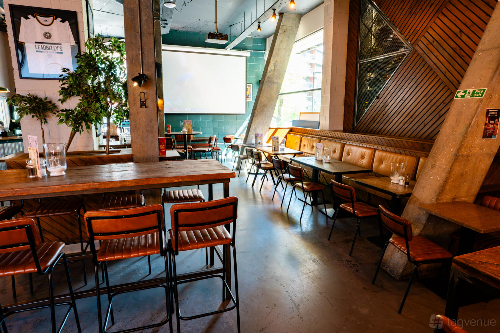 An event space in a bar with wooden tables, metal chairs, and a large projector screen at Leadbelly's Bar & Kitchen.