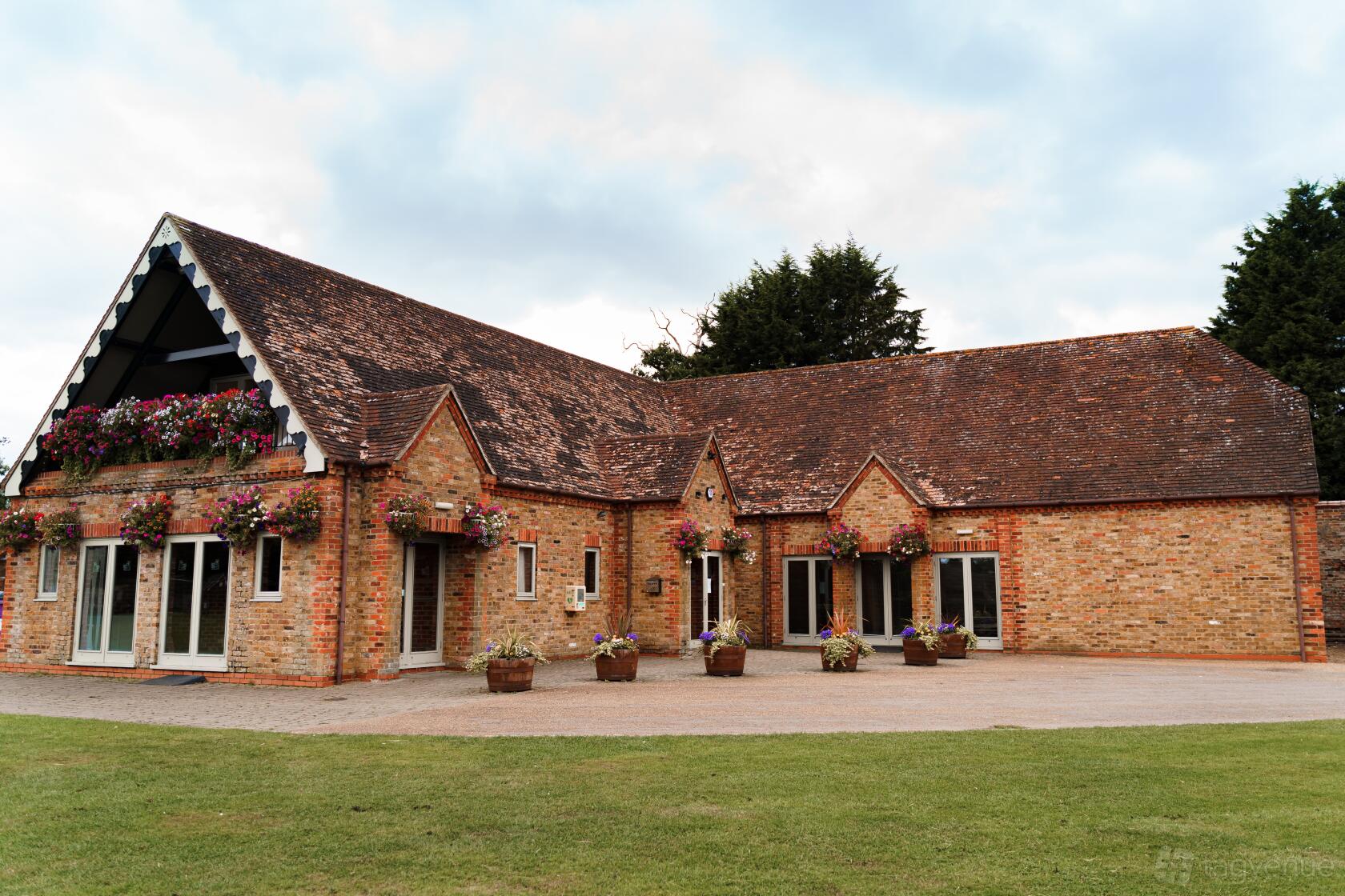 A brick hall with a pitched tiled roof, hanging flower baskets, and large windows at Eversholt Hall.
