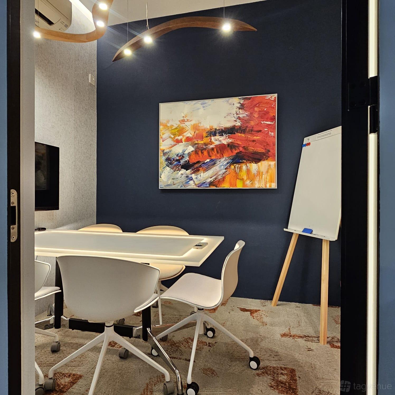 A meeting room with a rectangular table, white chairs, abstract wall art, and a flip chart stand at Dott Cowork.