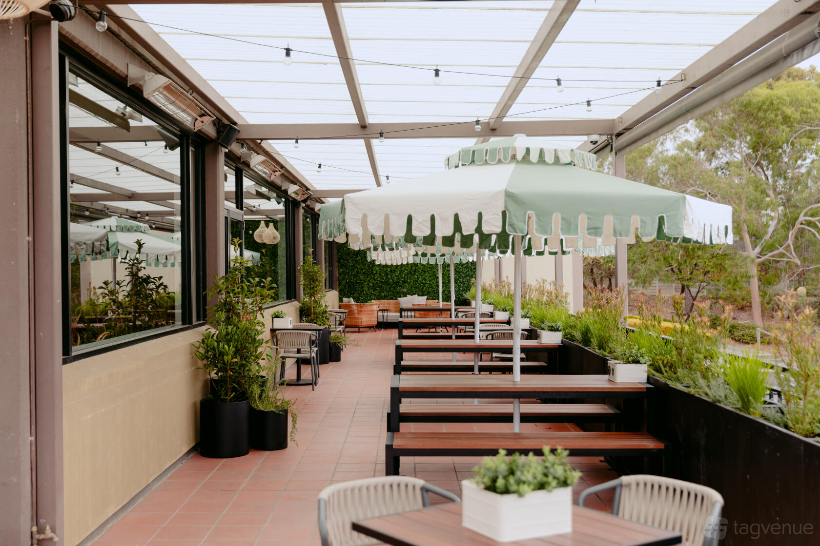 A pub terrace with wooden picnic tables, green striped umbrellas, and potted plants at Cherry Hill Hotel.