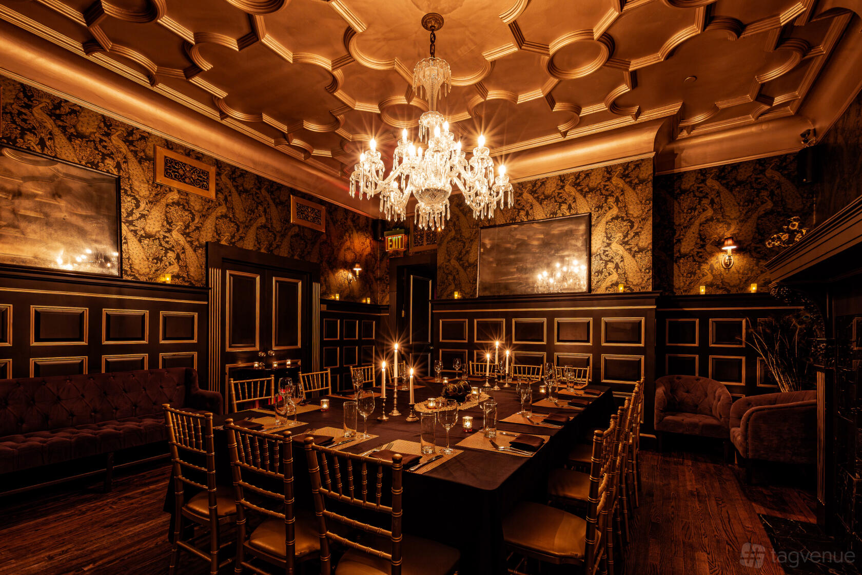 A function room with a crystal chandelier, candlelit banquet table, and patterned wallpaper at The Raines Law Room at The William.