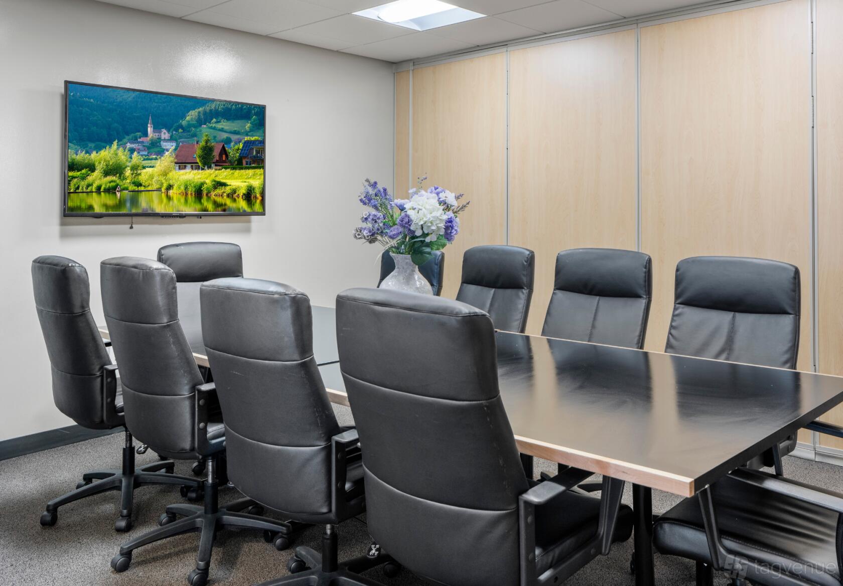 A boardroom with a glass-topped table, black leather chairs, and wall-mounted TV at Intelligent Office.