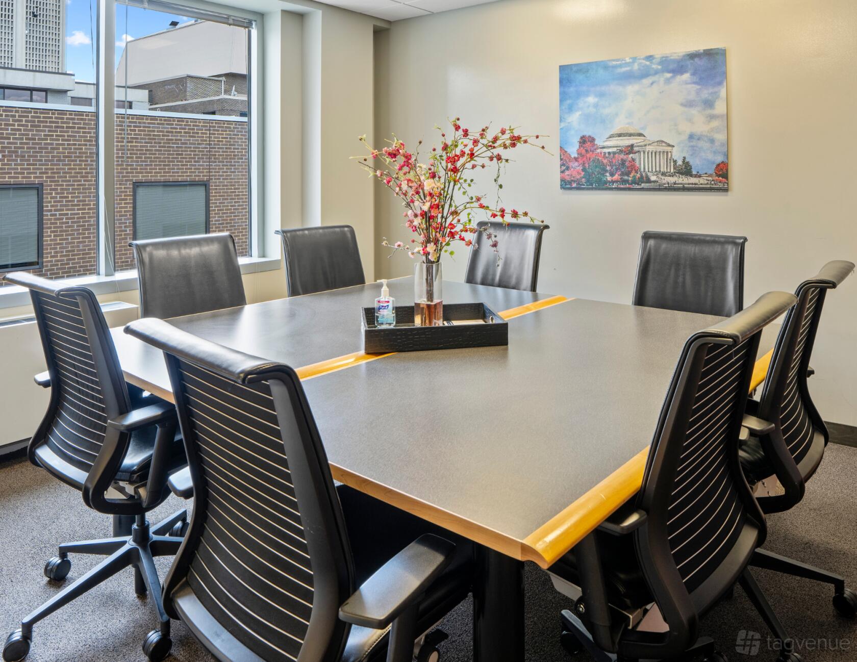 A meeting room with a rectangular table, black chairs, a vase of flowers, and natural light at Intelligent Office.