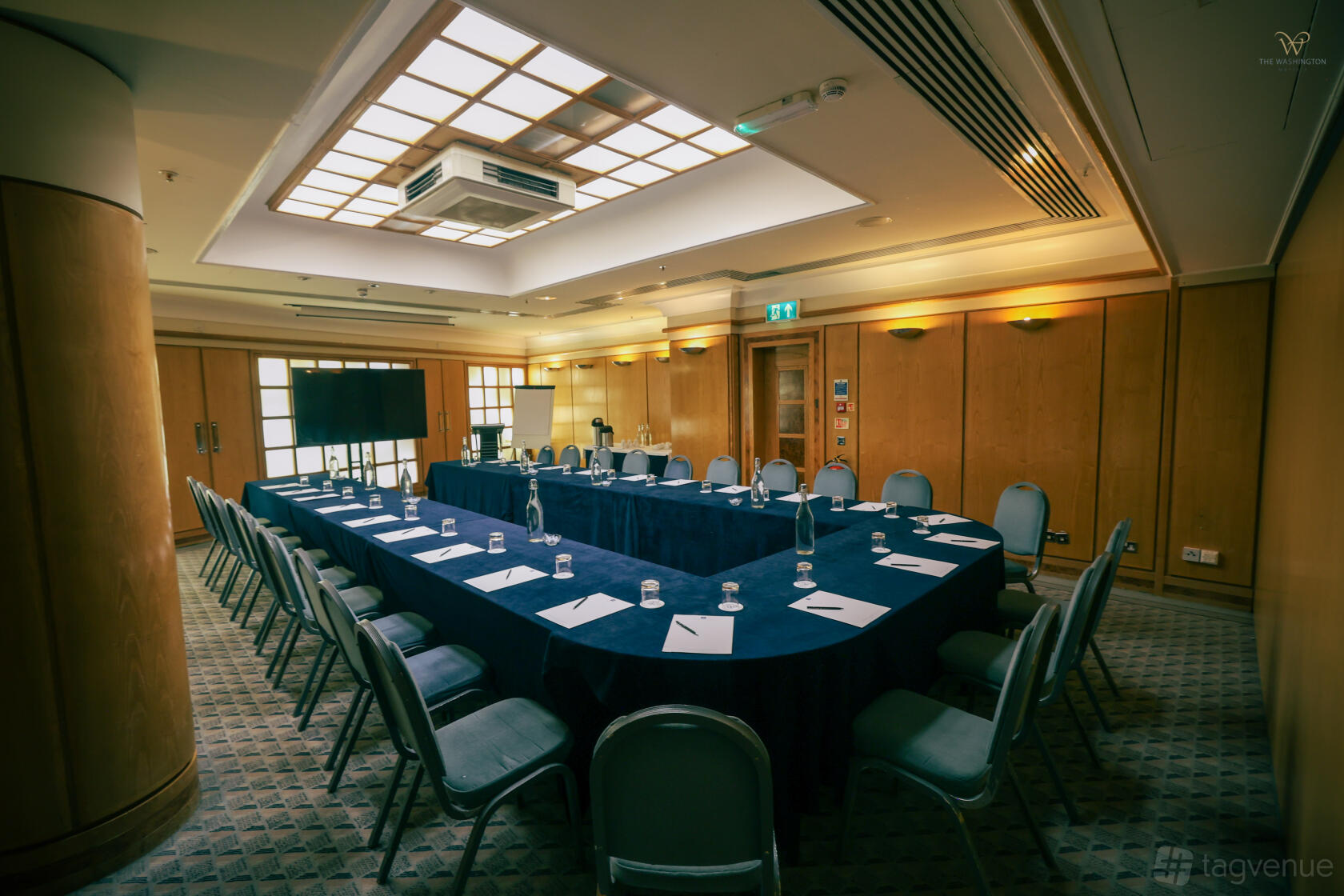 An event space with U-shaped conference tables, blue chairs, and a tray ceiling with recessed lighting at The Washington Mayfair Hotel.