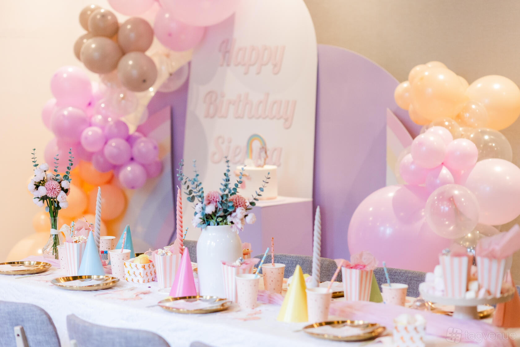 A hotel event room with pastel balloon decorations, a long table set for a birthday party, and fresh floral centerpieces at DoubleTree by Hilton London Kensington.