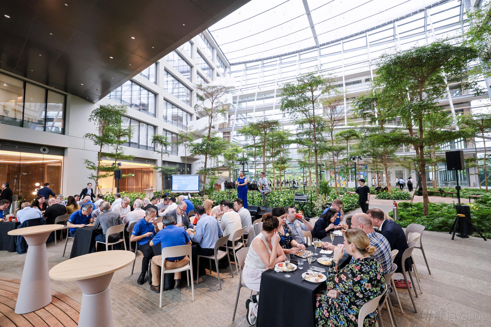 An event space with lush greenery, glass ceiling, and group seating at Surbana Jurong Campus