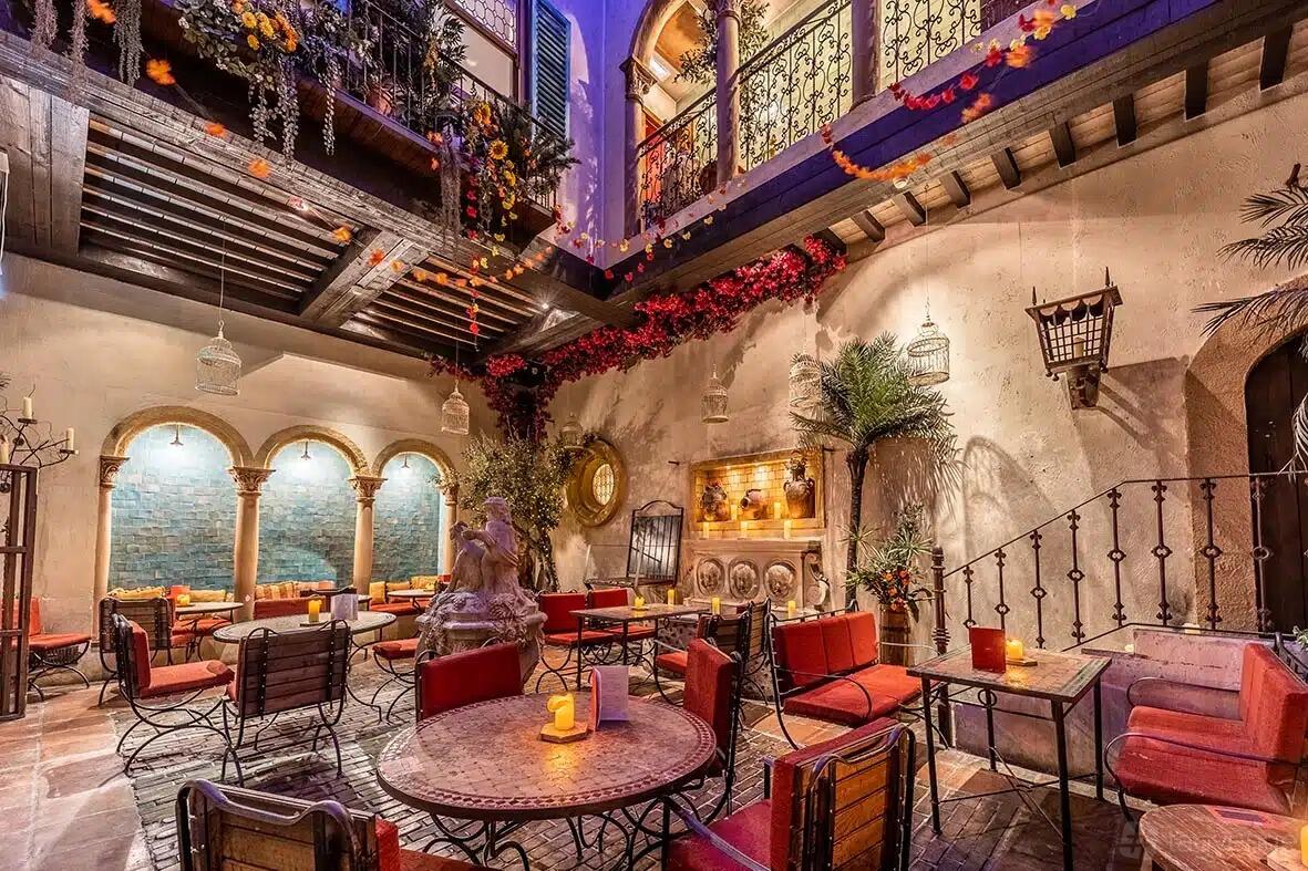 A courtyard function room with wrought iron chairs, round tables, and floral garlands at Arta.