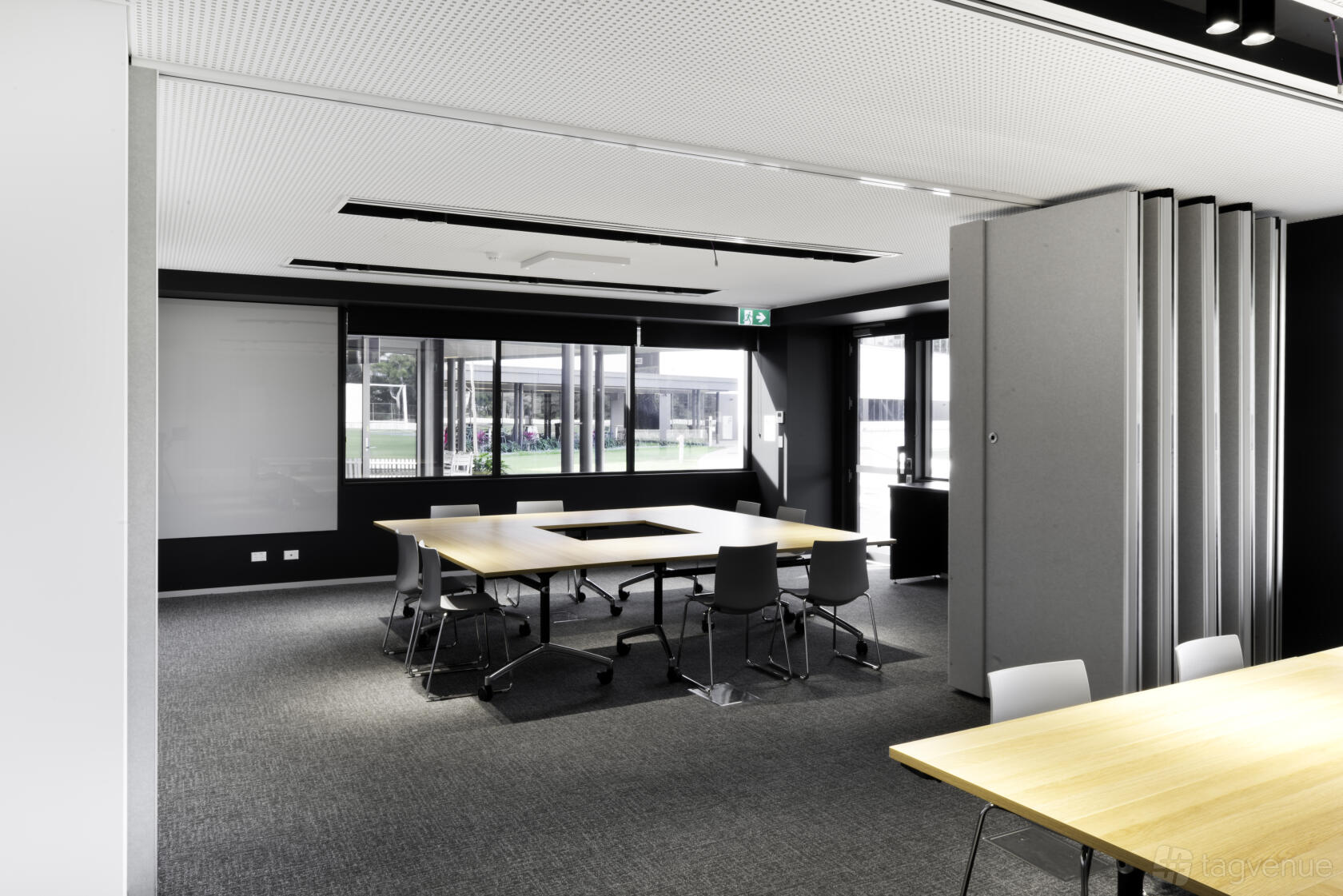 A meeting room with modular tables arranged in a U-shape, sliding partition walls, and floor-to-ceiling windows at Cricket Central.