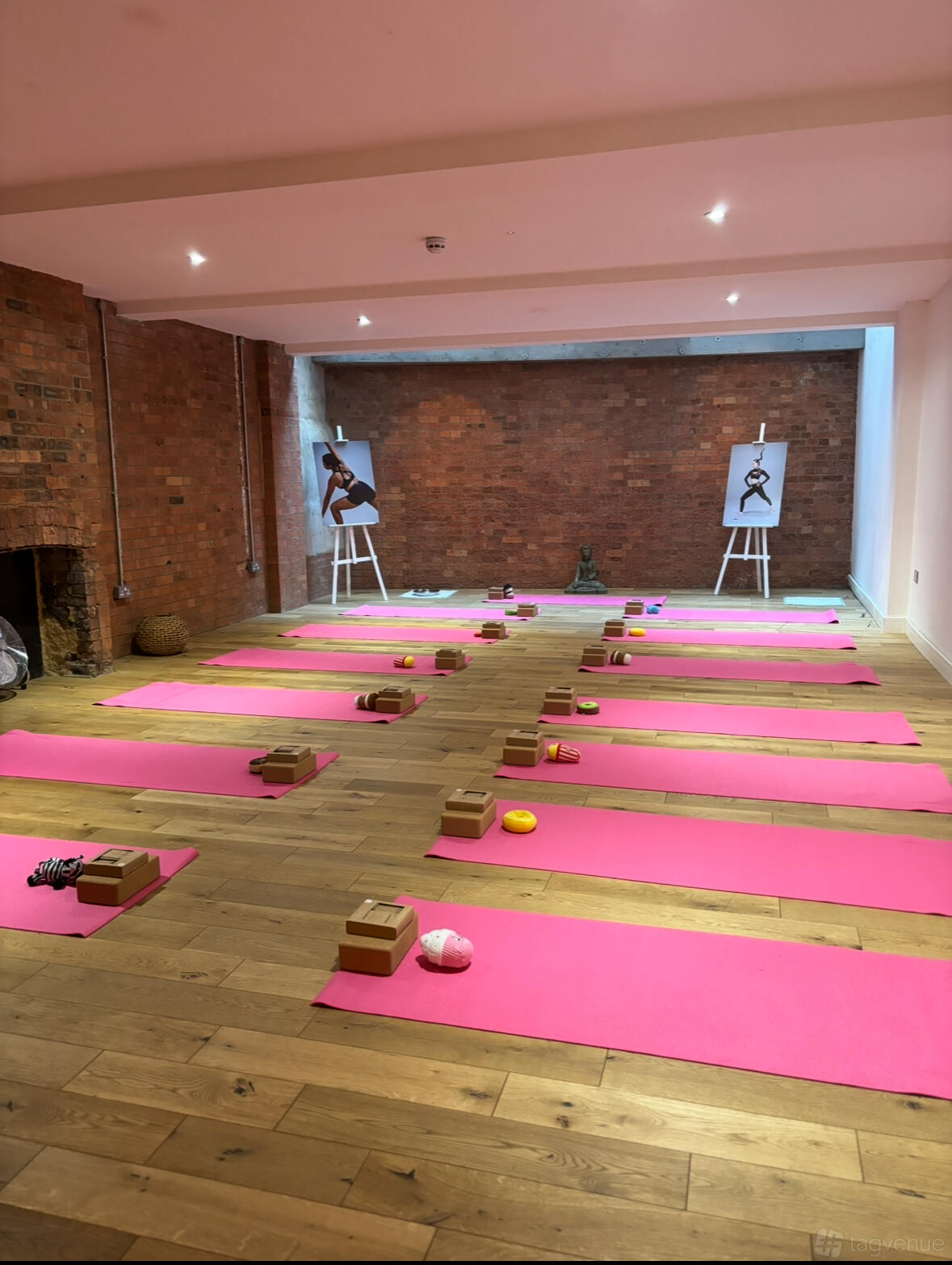 A yoga studio with exposed brick walls, pink mats, and yoga props arranged on wooden floors at Serenity Studio London.