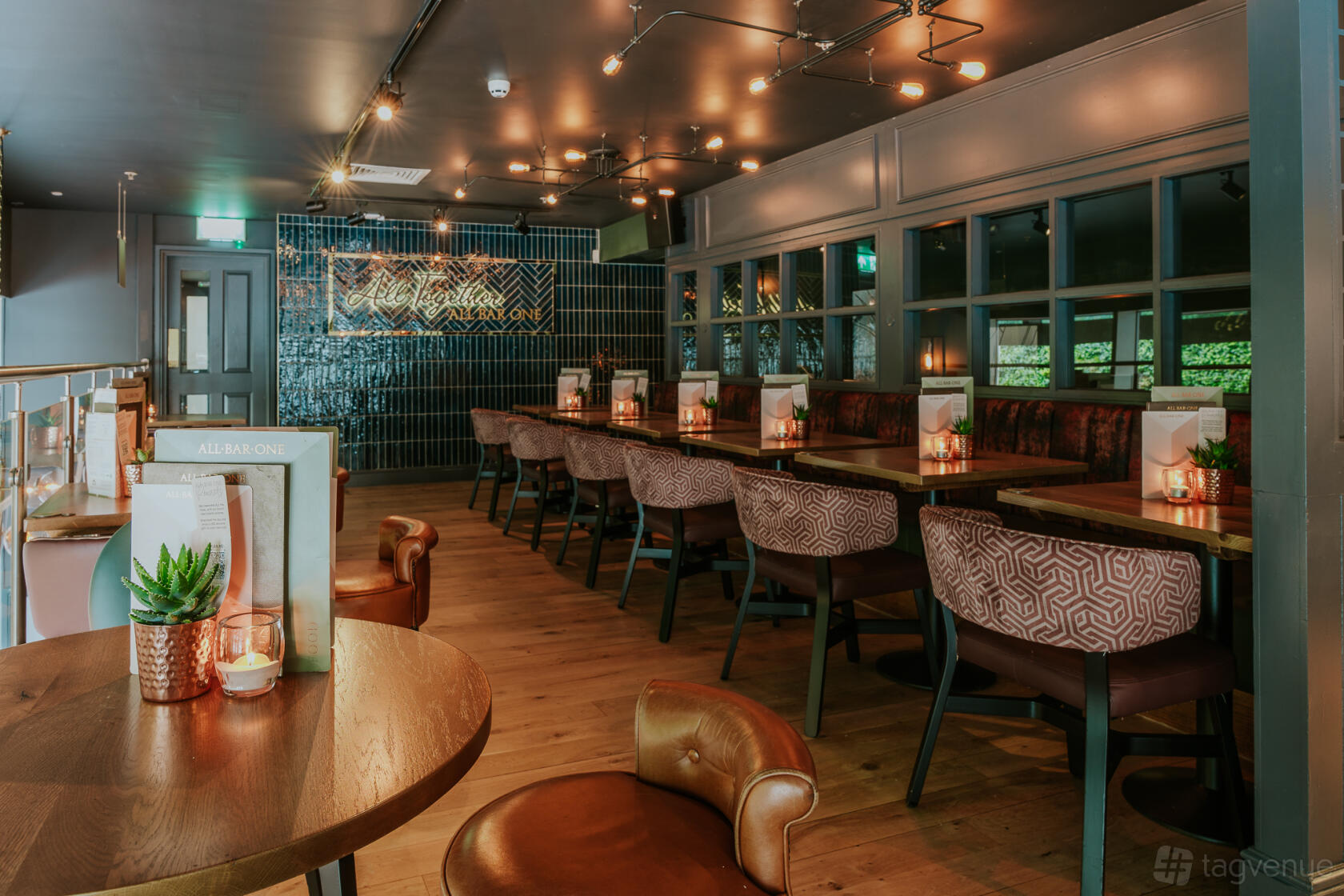 An event space in a bar with wooden flooring, booth seating, patterned chairs, and ambient lighting at All Bar One Victoria.