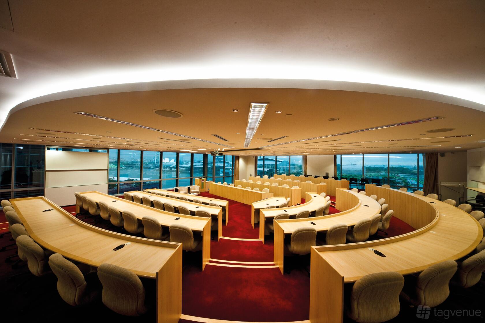 A conference centre meeting room with curved rows of desks, swivel chairs, and floor-to-ceiling windows at NTUC Centre.