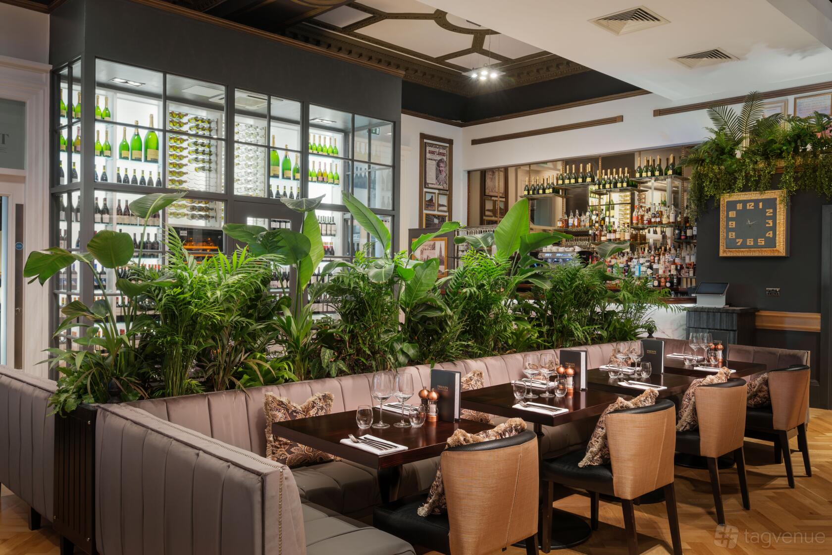 A restaurant with cushioned banquette seating, lush potted plants, and a glass wine display at Hotel Indigo Edinburgh - Princes Street.