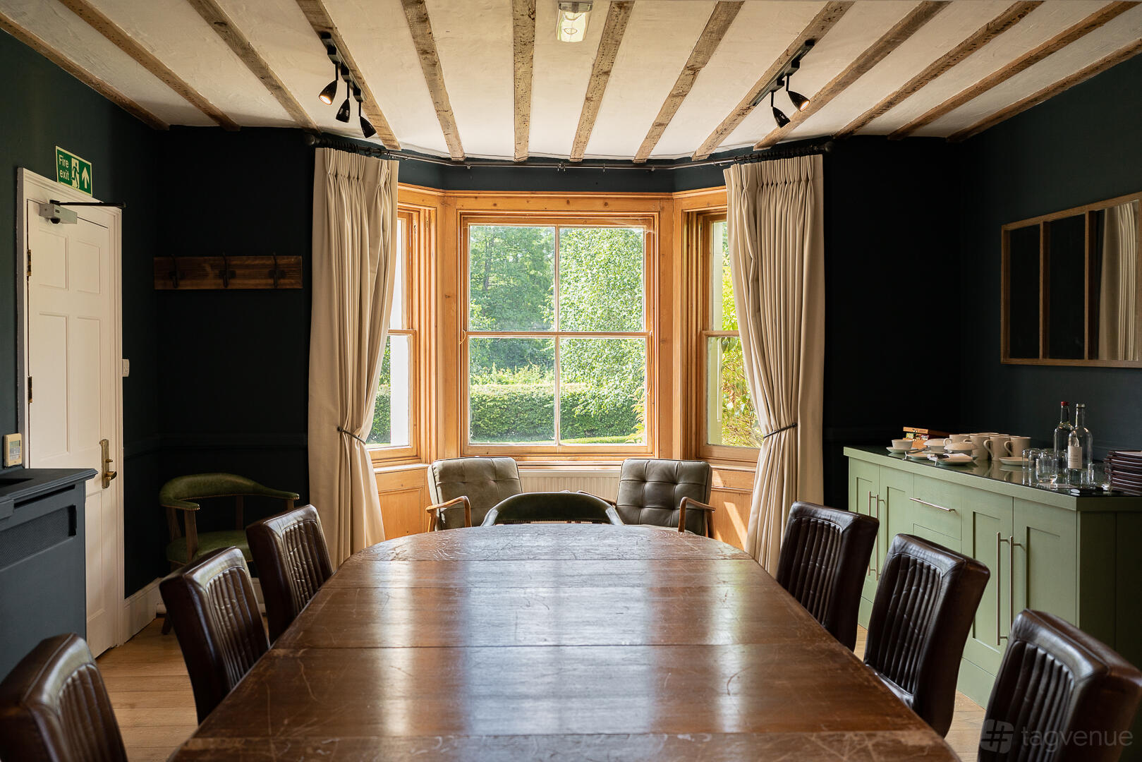 A boardroom with a large wooden table, leather chairs, and bay window with garden view at Tewinbury Farm Hotel.