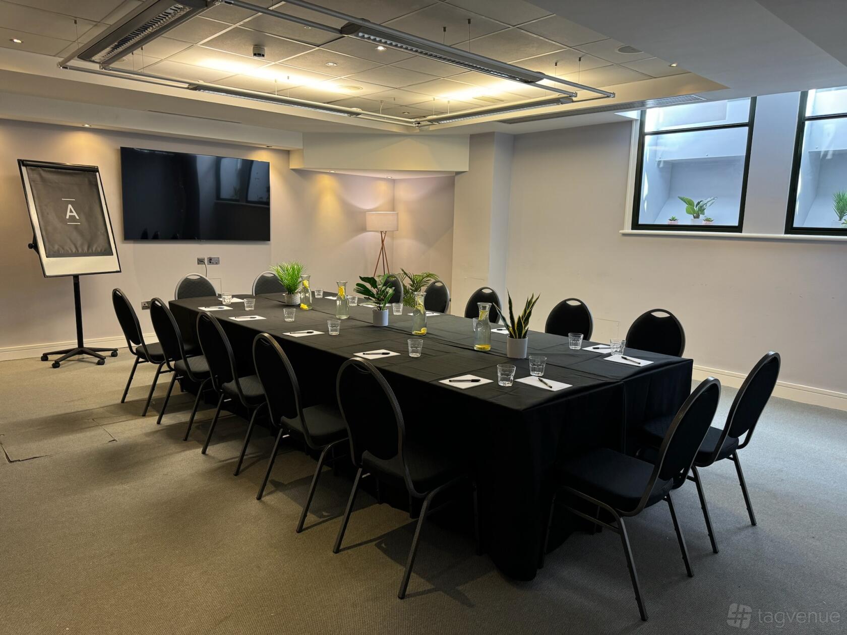 A meeting room with a rectangular table, black chairs, notepads, water glasses, and natural light at The Alan.