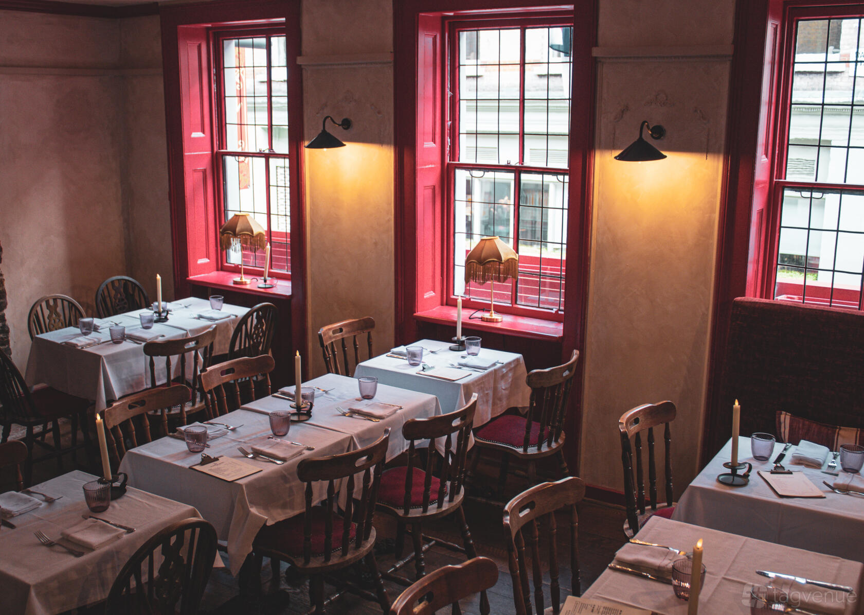 A dining room in a pub with wooden chairs, white-clothed tables, and tall windows at The Newman Arms.
