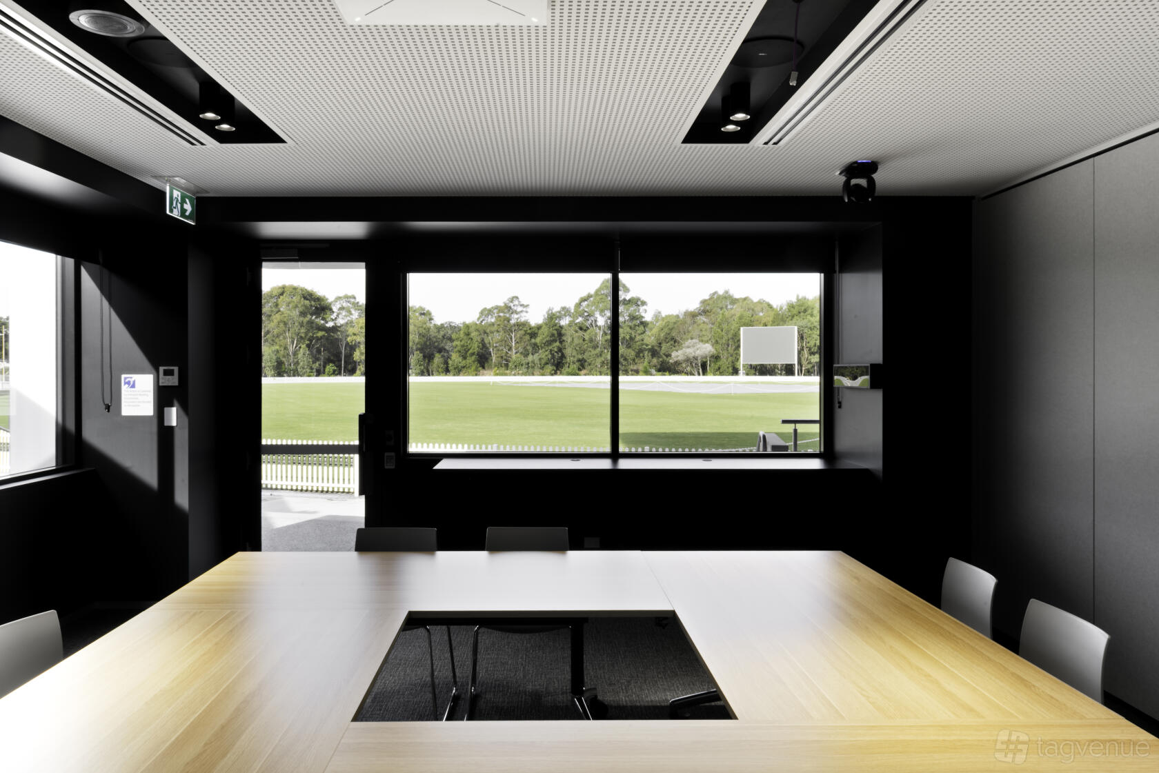 A meeting room with a square wooden conference table, floor-to-ceiling windows, and field views at Cricket Central.