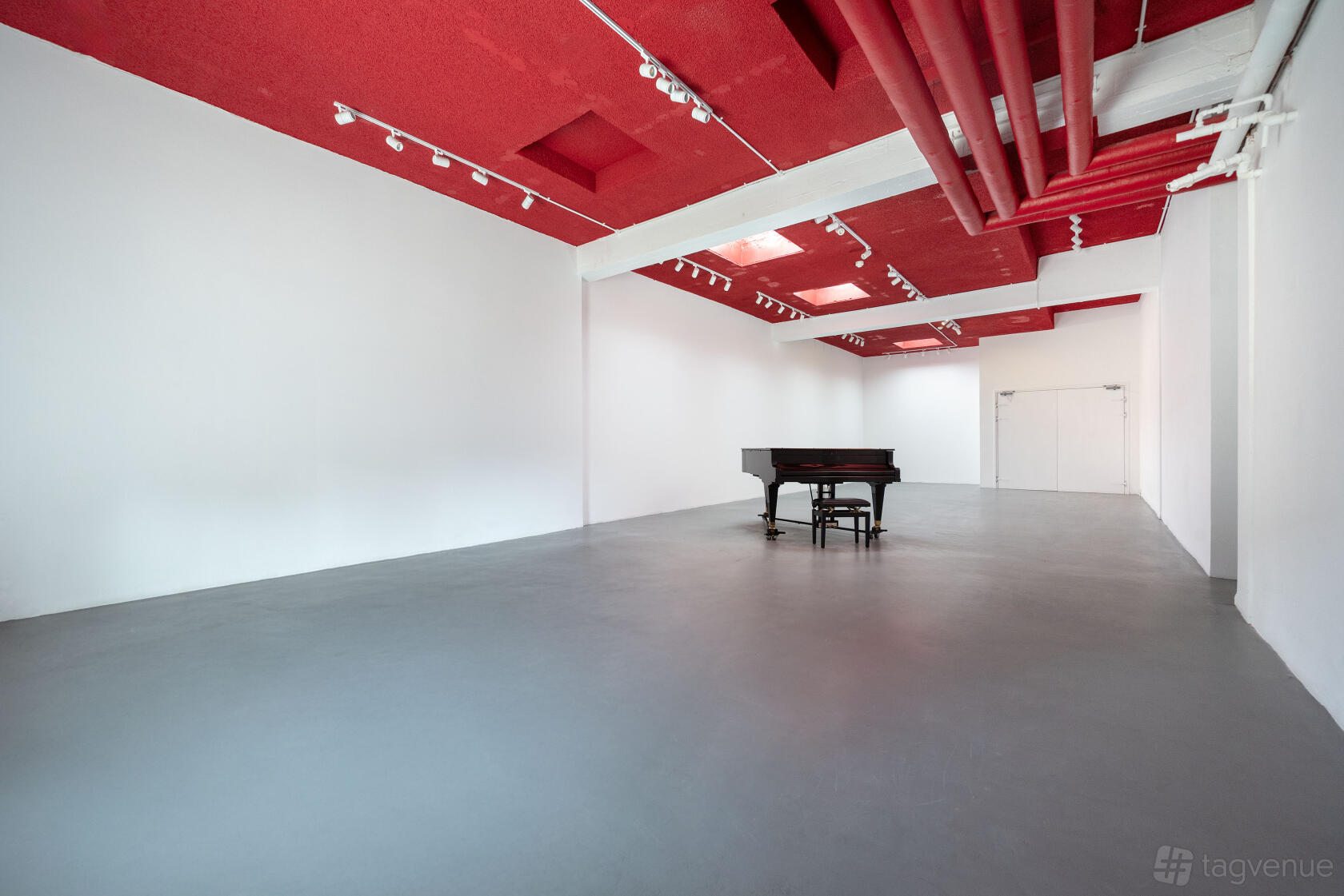 An event venue with a red ceiling, exposed pipes, skylights, and a black grand piano at Proposition Studios.