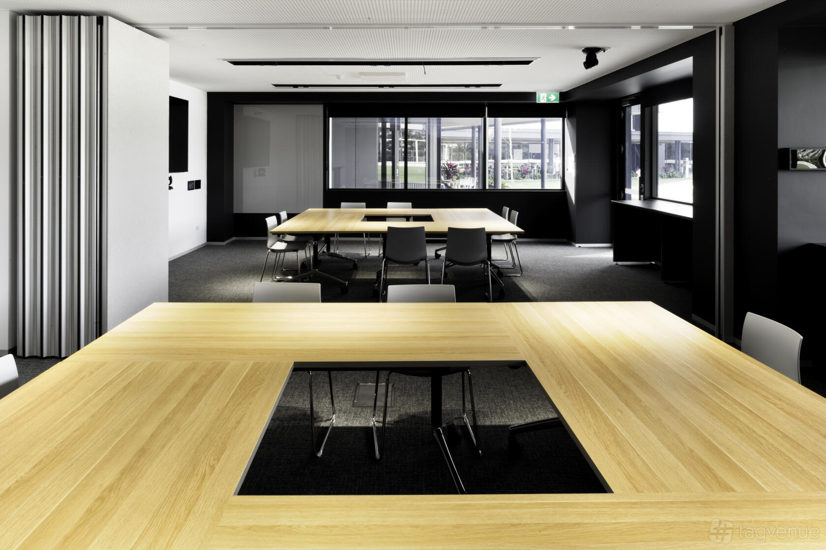 A meeting room with modular light wood tables arranged in a U-shape and large windows at Cricket Central.