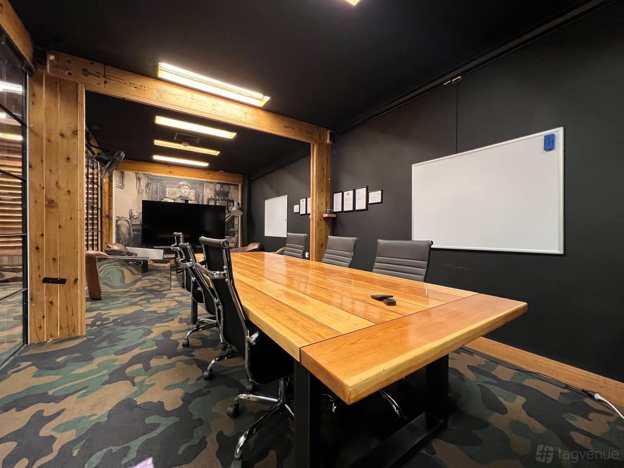 A meeting room with a wooden conference table, black chairs, wall-mounted whiteboard, and TV at DeskPlex Coworking.